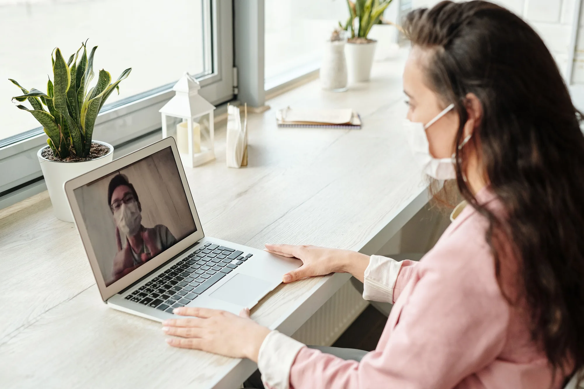 A woman having a video consultation with a masked clinician visible on her laptop screen.